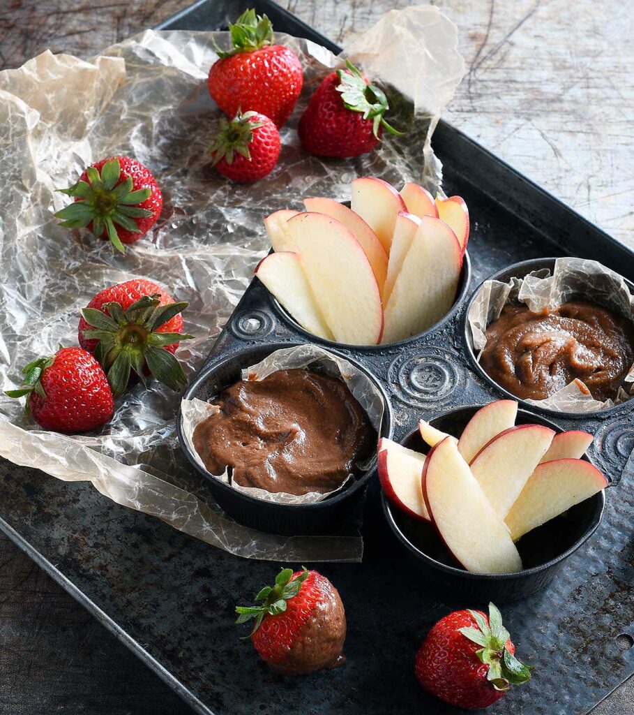 Chocolate hummus and caramel hummus in an old muffin tin with slices apples and strawberries for dipping.