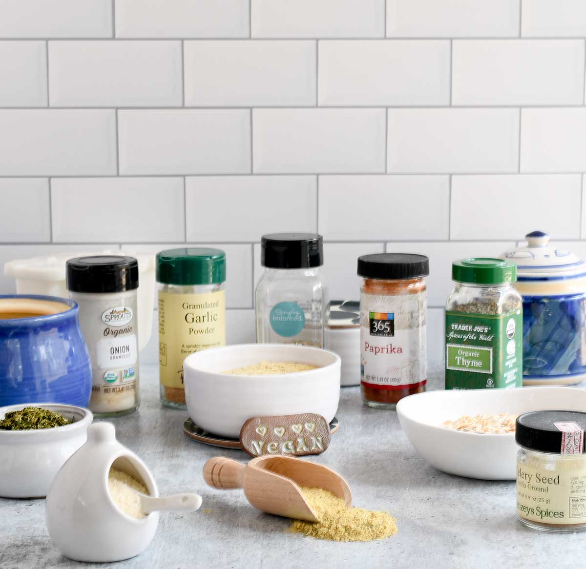 Bottles of herbs, spices, and other ingredients needed to make vegan chicken broth powder. On a grey  concrete countertop. 