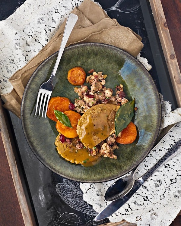 Vegan Thanksgiving dinner of sliced seitan and gravy, stuffing with cranberries, and sweet potatoes on a green plate.
