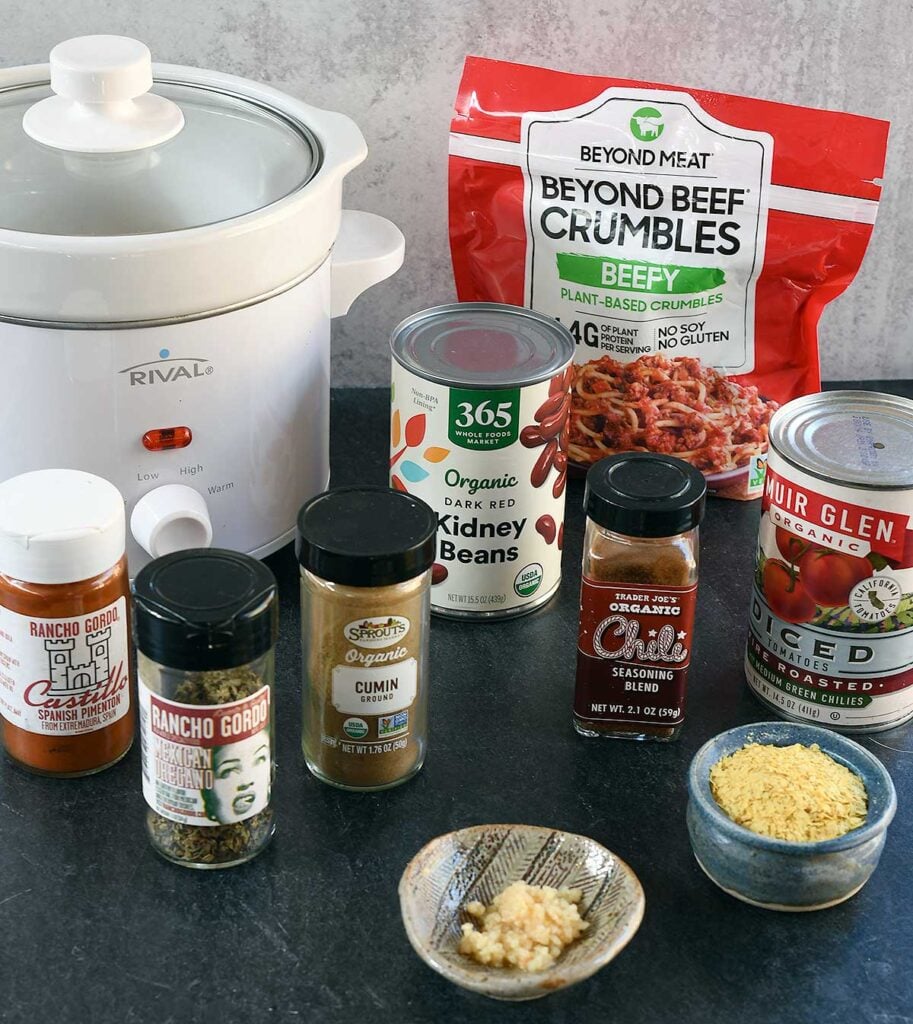 A white 2-quart slow cooker surrounded by Beyond Meat vegan beef crumbles, and the other ingredients needed for this chili.