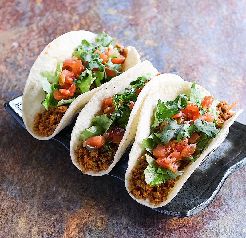 Soft tacos with minced soy curl filling topped with lettuce, chopped tomatoes, and cilantro.