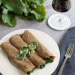 3 gluten-free teff crepes on a white plate with a fork and a wine glass on the side