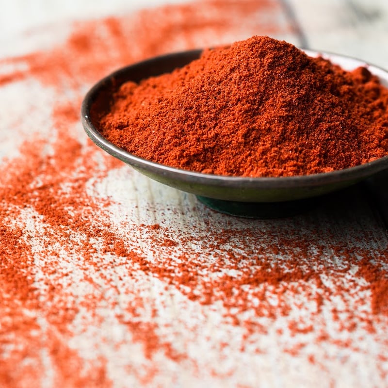 Ground paprika in a small saucer with scattered grains on the table